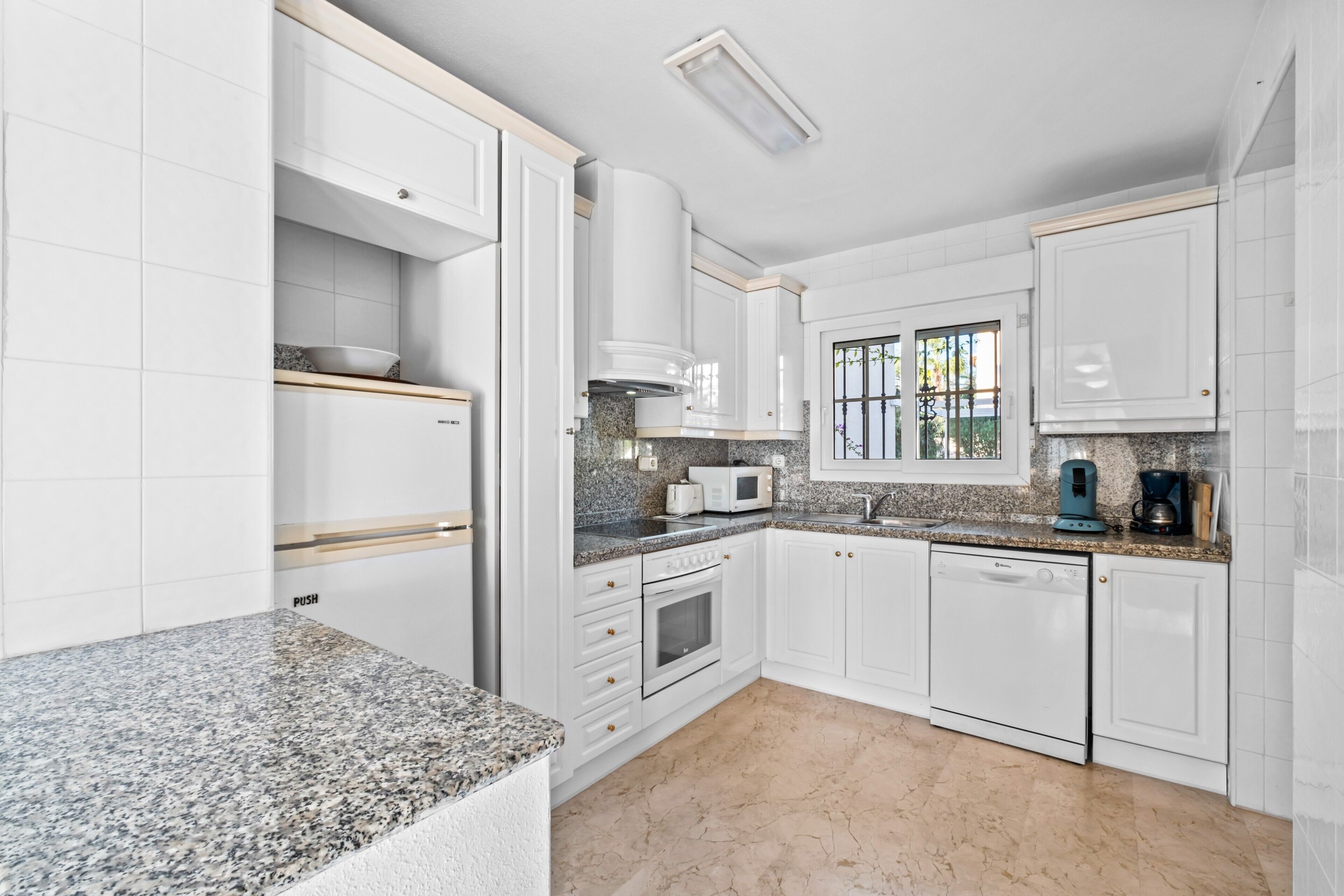 A kitchen with white cabinets, granite countertops, a built-in oven, a microwave, and a coffee maker.