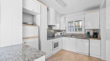 A kitchen with white cabinets, granite countertops, a built-in oven, a microwave, and a coffee maker.