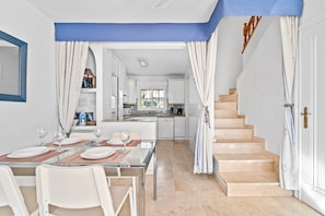 A modern kitchen with white cabinets, a dining area with a glass table, and a staircase leading to an upper floor. - Holiday Home with Shared Pool, Terrace & Wi-Fi (Orihuela)