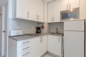 A compact kitchen with white cabinets, a built-in microwave, a coffee maker, and a toaster.
