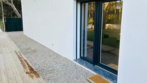 En moderne bygning med hvid facade, træterrasse og skydedør, der fører til et overdækket udeområde.