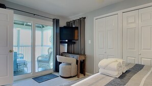 Une chambre à coucher comprenant un lit, une télévision, un bureau et une porte-fenêtre coulissante donnant sur un balcon.