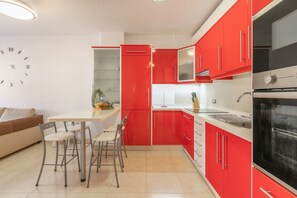 Une cuisine moderne avec des meubles rouges, un plan de travail blanc et un four encastré.