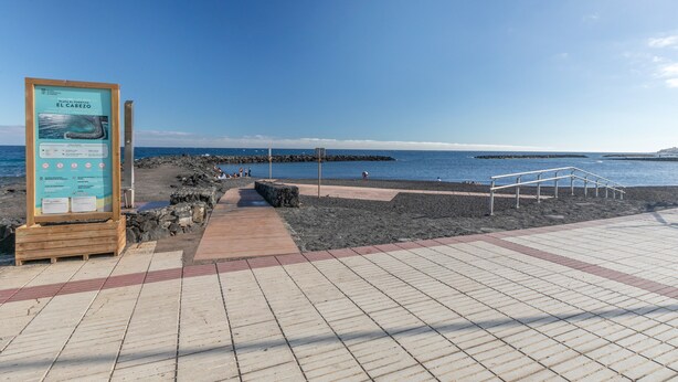A coastal walkway with a signboard, a wooden bench, and a metal railing. - Holiday Home 'Vista Mar' with Sea Views, Shared Pool and Wi-Fi (Puertito de Güímar)