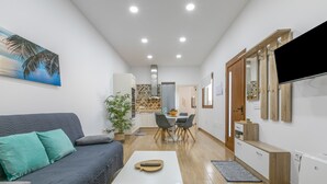 Una sala de estar moderna con un sofá, una mesa de centro, un televisor y una cocina al fondo.