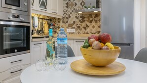 Una cocina equipada con microondas, horno y refrigerador. Hay un tazón de fruta sobre la mesa.
