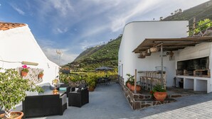 Un patio al aire libre con asientos, plantas en macetas y vistas a una ladera.