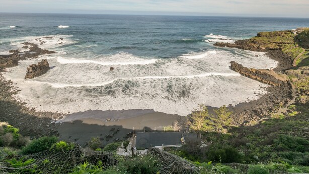 Paisaje costero con acantilados rocosos, una playa y un pequeño edificio.