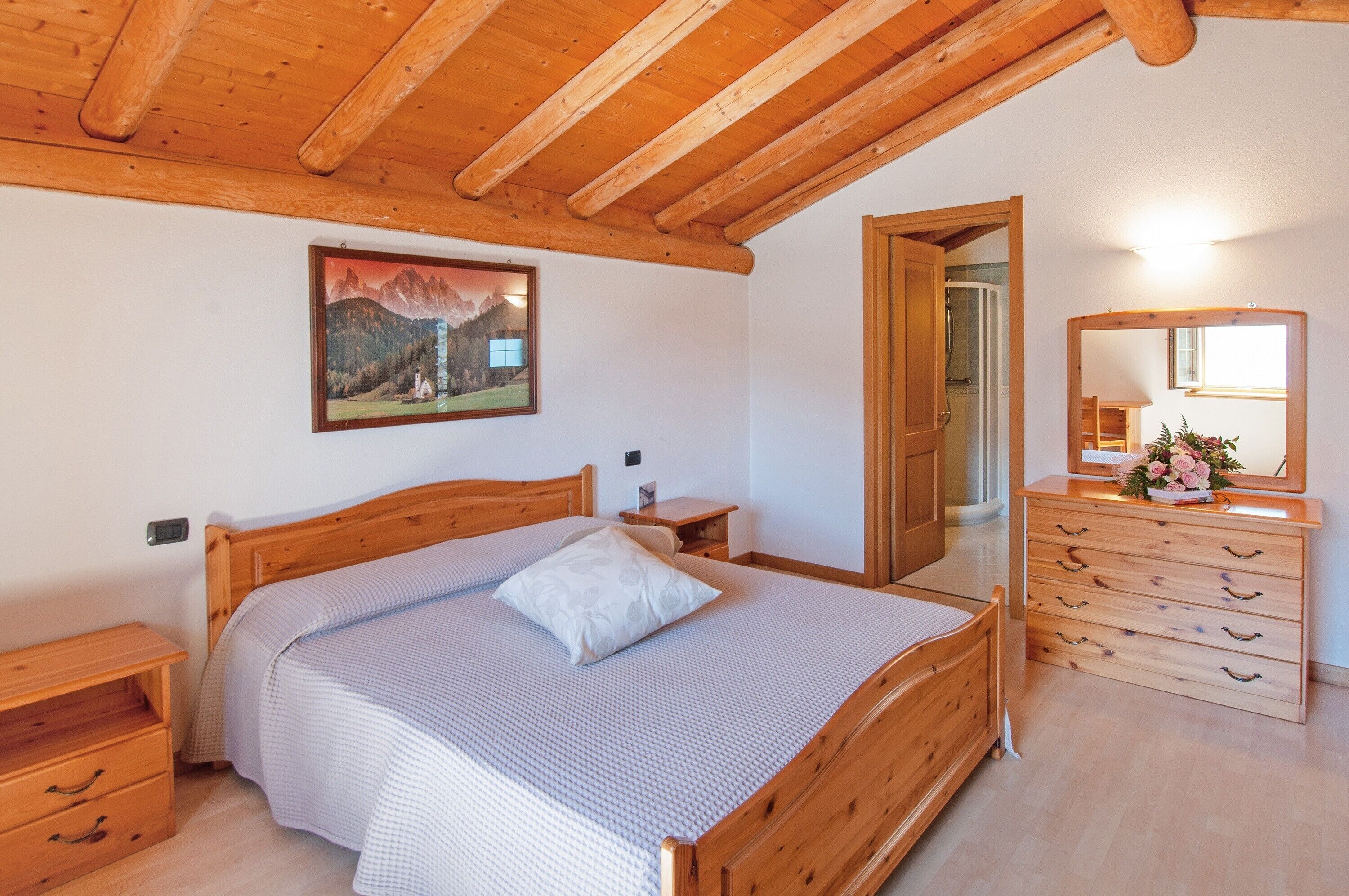 A bedroom with a wooden bed, a nightstand, a dresser, a mirror, and a painting on the wall.