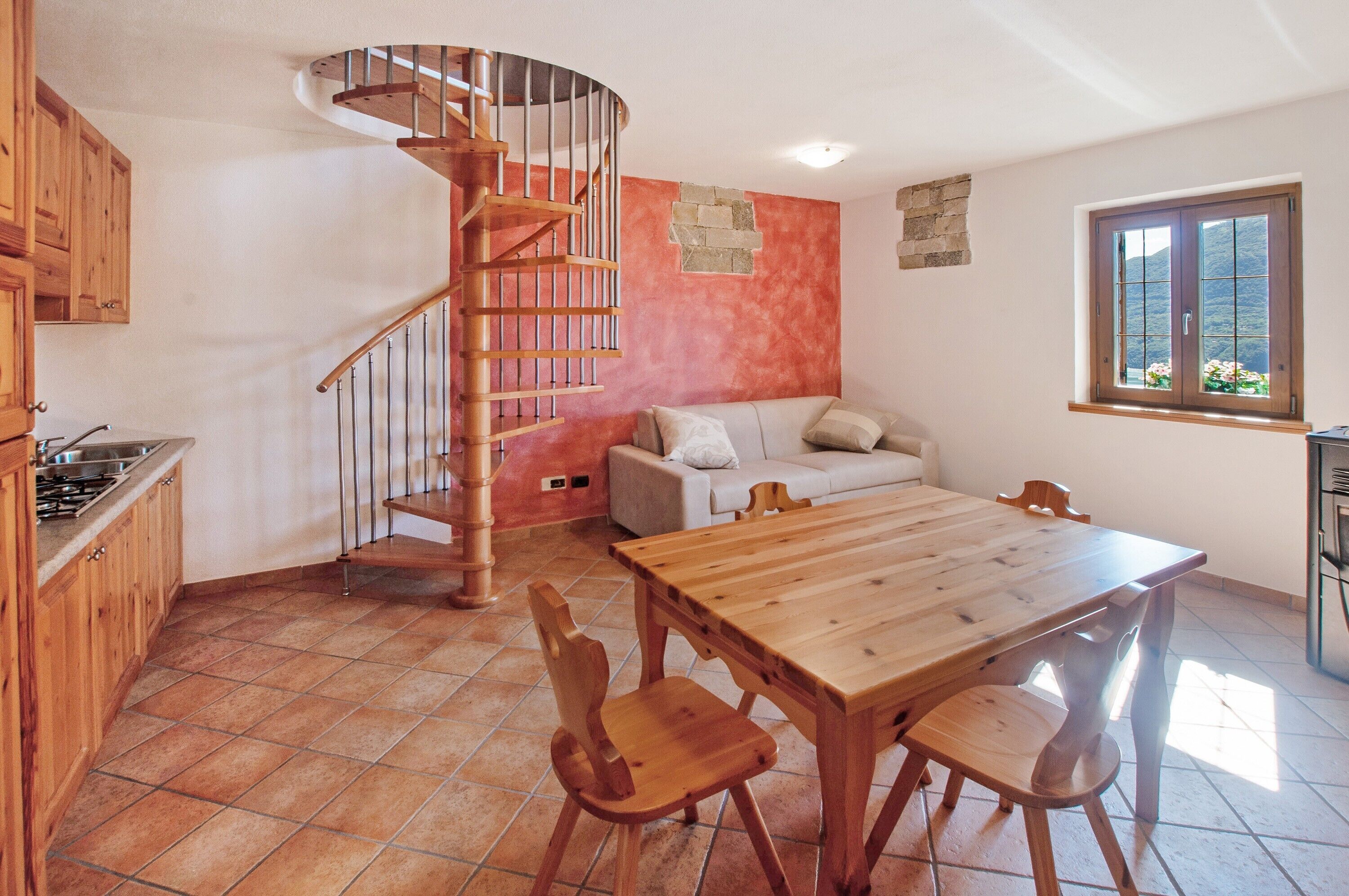 A kitchen with a wooden table and chairs, a spiral staircase, a sofa, and a window with a view.