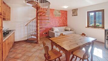 A kitchen with a wooden table and chairs, a spiral staircase, a sofa, and a window with a view.