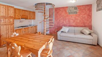 Eine Küche mit Holzausstattung, einem Esstisch mit Stühlen, einem Einbauherd und einer Wendeltreppe.