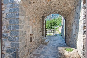 A stone pathway leading through an arched doorway, flanked by stone walls, with a view of greenery and a mountain in the distance. - Holiday Home Il ciliegio sul lago with Lake View, Terrace, and Garden (Verceia)