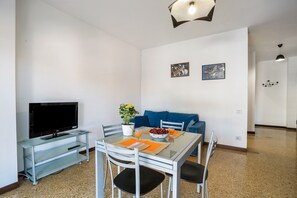 A dining area with a glass table, chairs, a TV on a stand, a potted plant, and a blue sofa. - Iris Apartment Lago Maggiore with Lake View, Balconies, Air Conditioning & Wi-Fi (Angera)