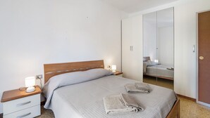 Una cama bien hecha con cabecera de madera, una mesita de noche con lámpara y un espejo grande en la pared.
