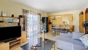 Un salon moderne doté d’un téléviseur à écran plat, d’une table basse en verre, d’un canapé et d’un coin repas avec une table et des chaises.