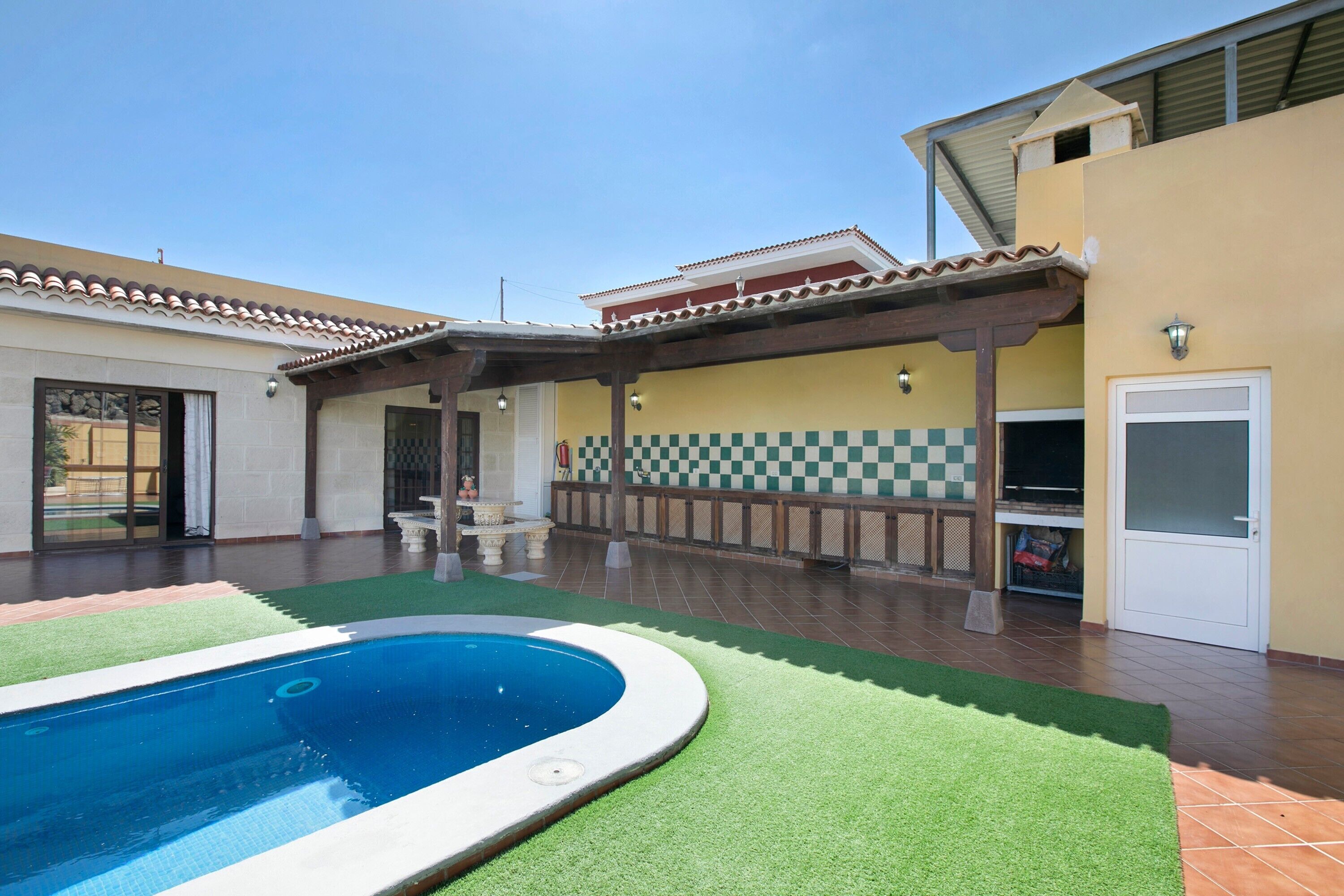Una piscina con césped artificial, un porche cubierto y un diseño de pared a cuadros.