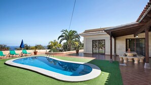 Une piscine bordée d’une pelouse verdoyante, un patio avec une table et des chaises, et une vue sur l’océan.