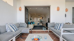 A modern living room with grey sofas, a coffee table with a fruit bowl, and a view into the dining area. - Apartment '2 Bed-rooms with A View' with Sea View, Wi-Fi and Air Conditioning (Benahavís)
