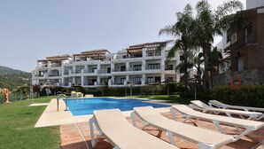 A poolside area with lounge chairs, a swimming pool, and a multi-story building with balconies. - Apartment '2 Bed-rooms with A View' with Sea View, Wi-Fi and Air Conditioning (Benahavís)