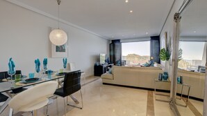 A modern living room with a dining area, a sofa, a TV, and a large window with a view. - Apartment '2 Bed-rooms with A View' with Sea View, Wi-Fi and Air Conditioning (Benahavís)