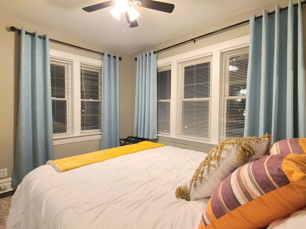 A bedroom with a bed, a ceiling fan, and windows with blinds.