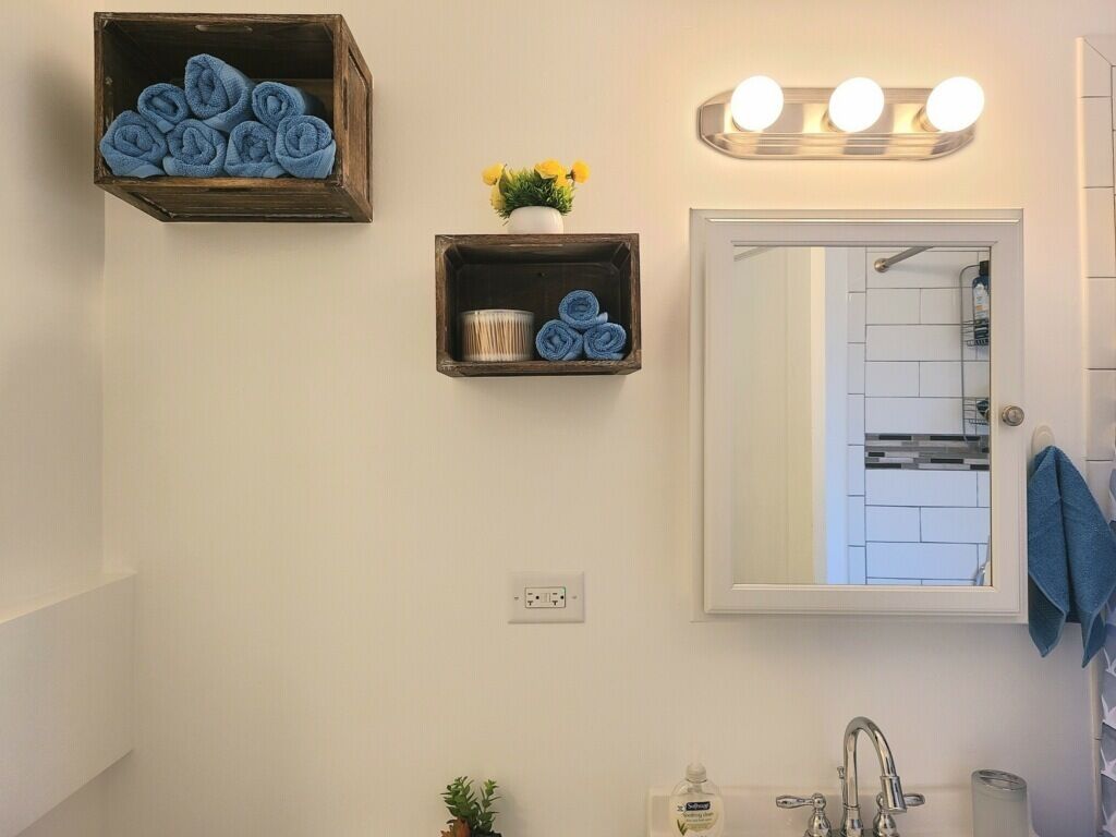 A bathroom with a mirror, a sink, and a shelf with towels and a plant.
