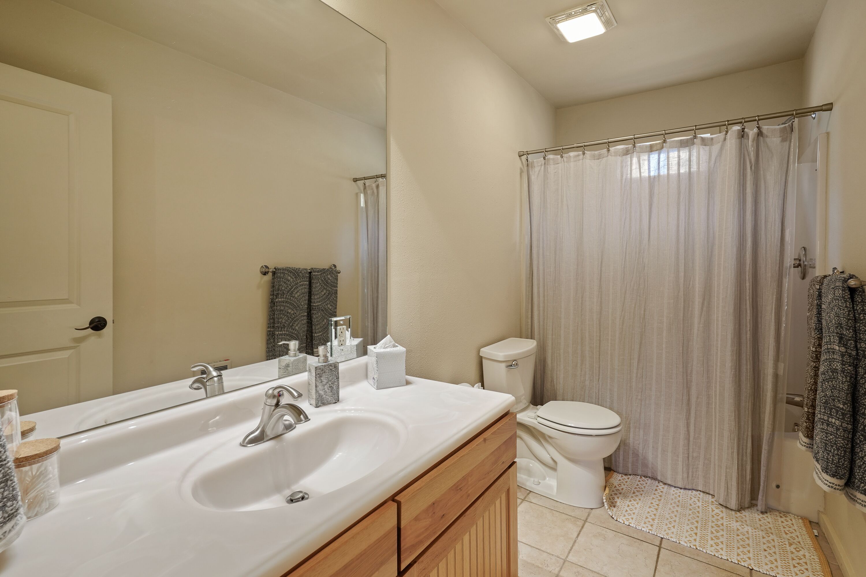 A bathroom with a white sink, mirror, toilet, and shower curtain.