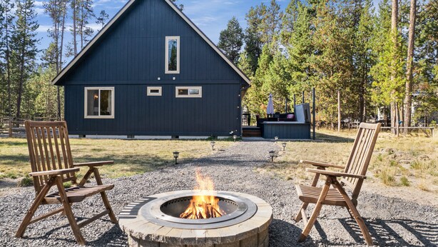 A cabin with a fire pit and two wooden chairs in front.