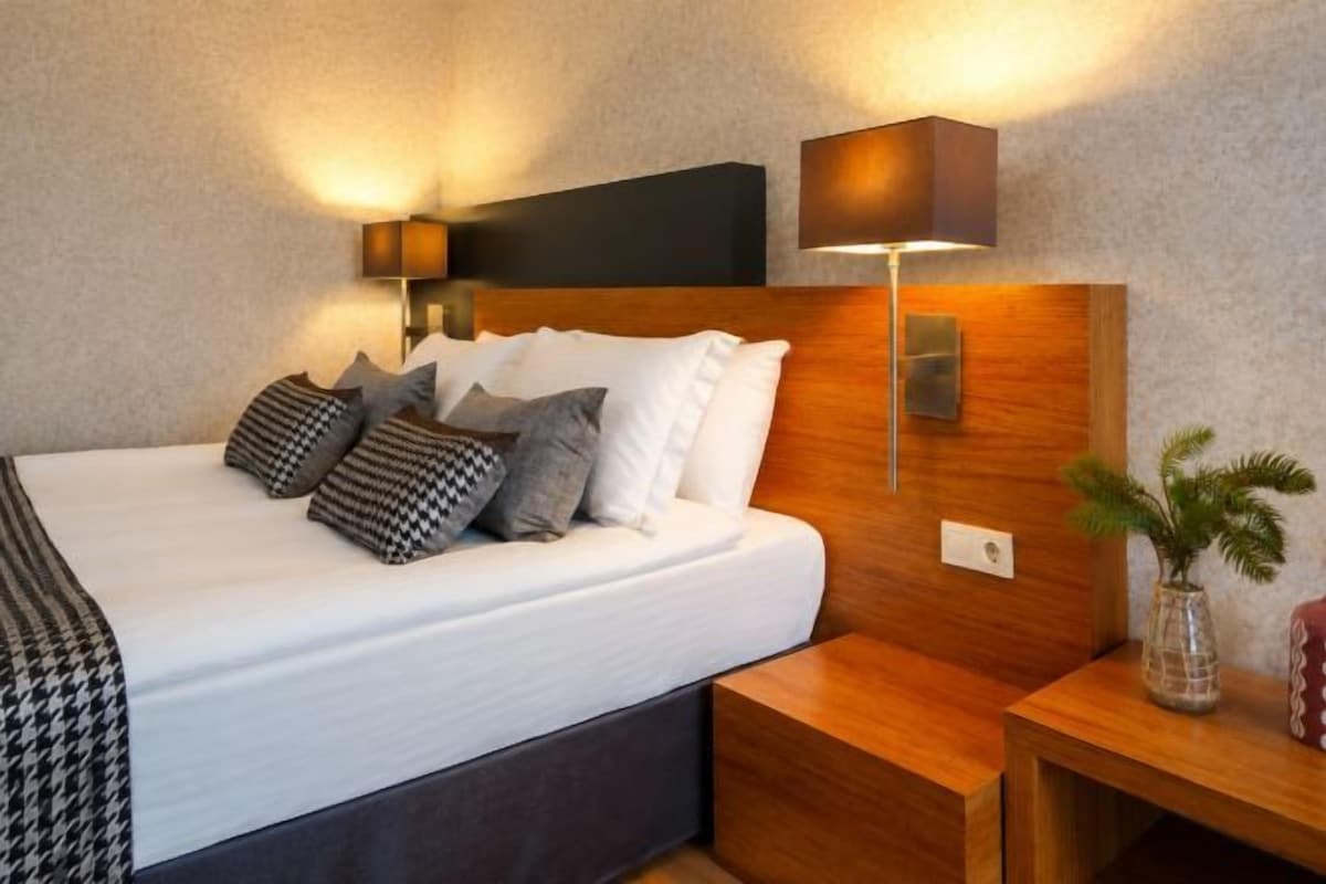 A hotel room with a large bed, bedside tables, a nightstand, and wall-mounted lamps.