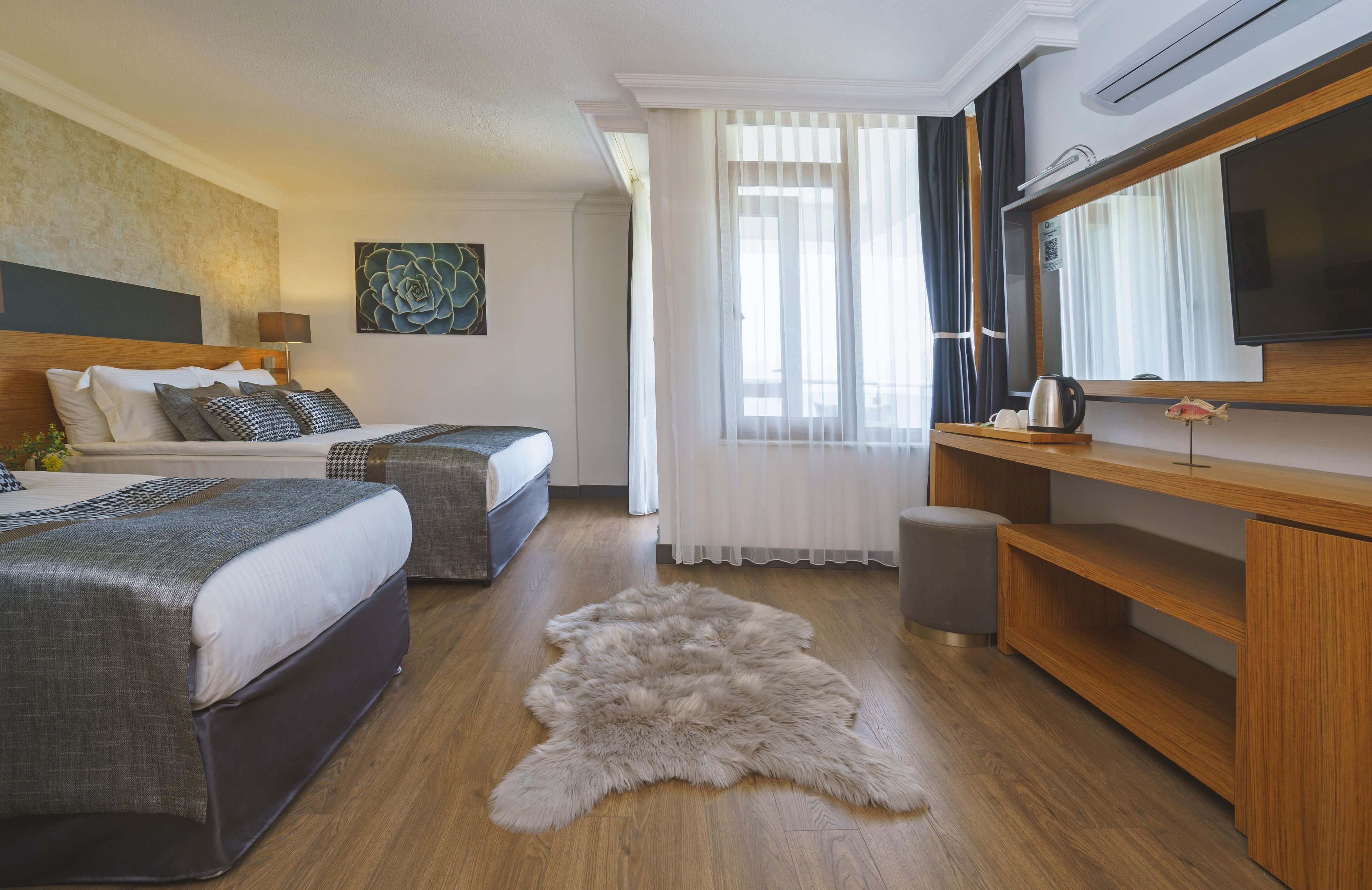 Habitación de hotel con dos camas, un televisor de pantalla plana grande, un escritorio de madera y un manto de piel en el suelo.