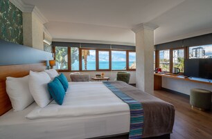 A hotel room with a large bed, a TV, a small table, and a view of the sea.