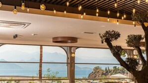 A restaurant with tables and chairs, a large tree, and a view of the sea. - Qinn Hotels (Antalya)