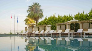 A pool area with lounge chairs and umbrellas, flags, and lush greenery. - Qinn Hotels (Antalya)