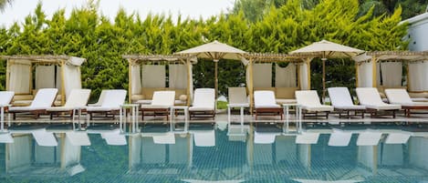 A pool with lounge chairs and umbrellas, surrounded by greenery.