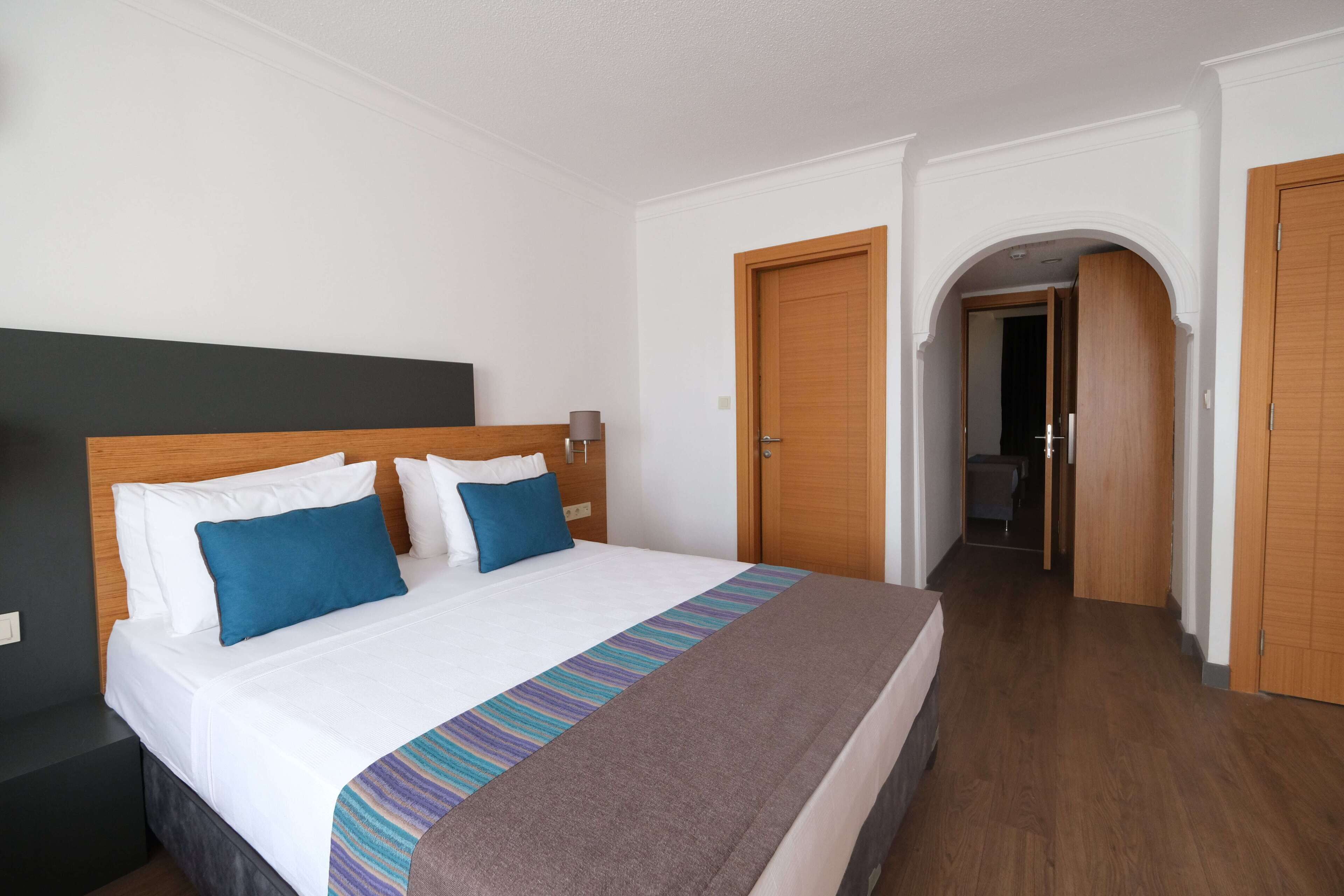 Habitación de hotel con una cama grande, cabecero de madera y vista al pasillo.