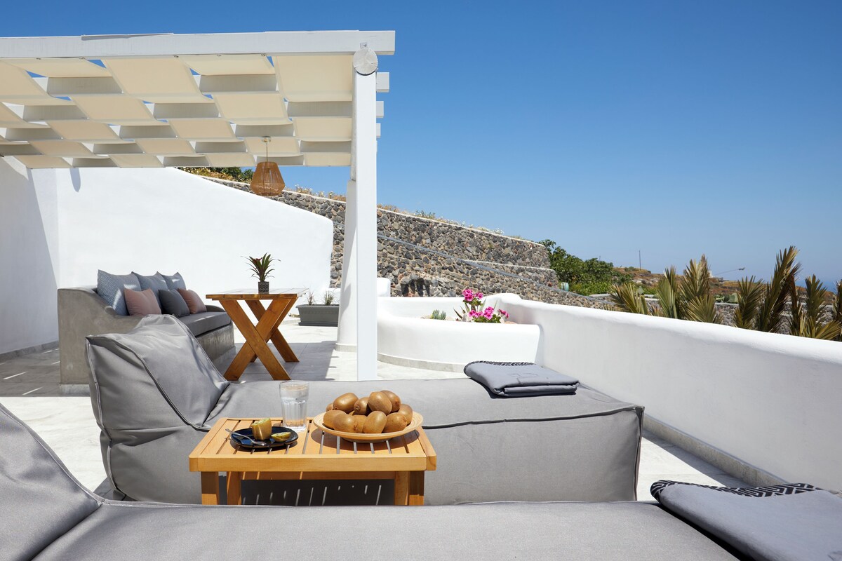 A modern outdoor seating area with a sofa, a wooden table with a fruit bowl, and a pergola structure.