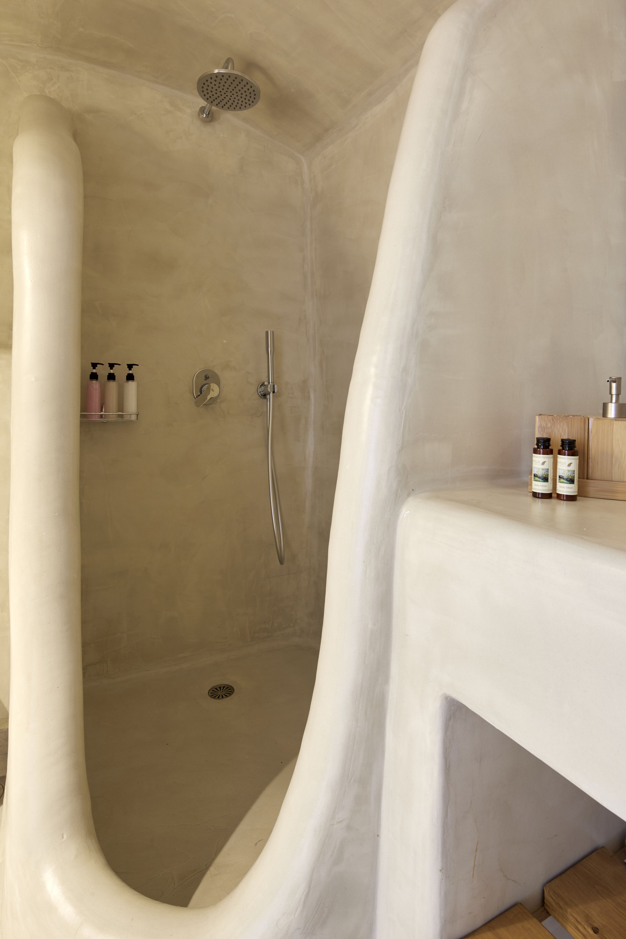 A shower with a curved design, a handheld showerhead, and a shelf with toiletries.