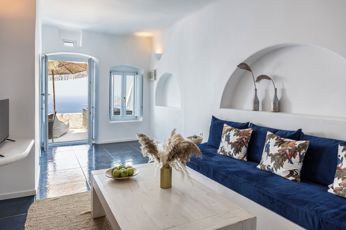 A modern living room with a blue sofa, a coffee table with decorative items, and a view of the sea through an open door.