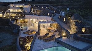 A luxurious villa with a swimming pool, outdoor seating, and stone walls. - El Verano Suites (Santorini)