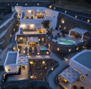A modern villa with a pool, outdoor seating, and stone walls. - El Verano Suites (Santorini)
