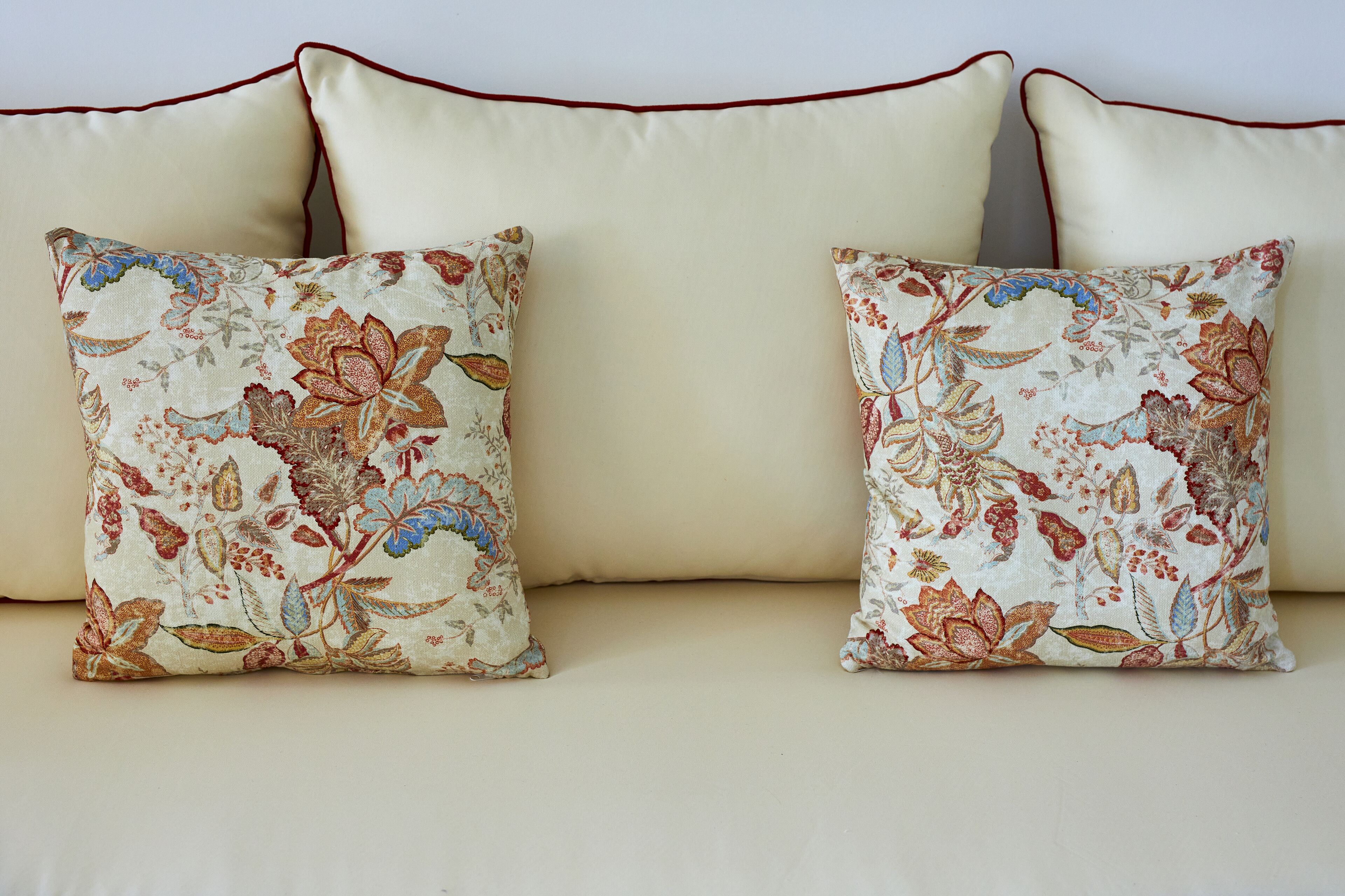Two floral-patterned pillows on a beige sofa with a red trim.