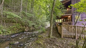 A wooden cabin with a deck overlooking a forested area and a stream. - #1 KID'S CABIN!! JUST RENOVATED| CREEK| MINI GOLF⛳️PIRATE PLAY SHIP🏴‍☠️ HOT TUB (Cosby)