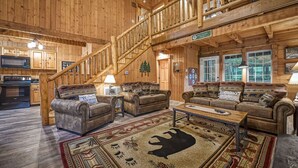 A spacious log cabin interior with a central seating area, a staircase, and a view of the surrounding forest. - #1 KID'S CABIN!! JUST RENOVATED| CREEK| MINI GOLF⛳️PIRATE PLAY SHIP🏴‍☠️ HOT TUB (Cosby)