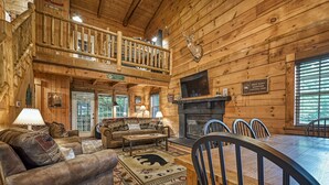 A log cabin interior with a fireplace, a dining table, and a sofa. - #1 KID'S CABIN!! JUST RENOVATED| CREEK| MINI GOLF⛳️PIRATE PLAY SHIP🏴‍☠️ HOT TUB (Cosby)
