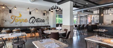 Un interior de restaurante con mesas dispuestas para comer, una zona de bar y una cocina a la vista.