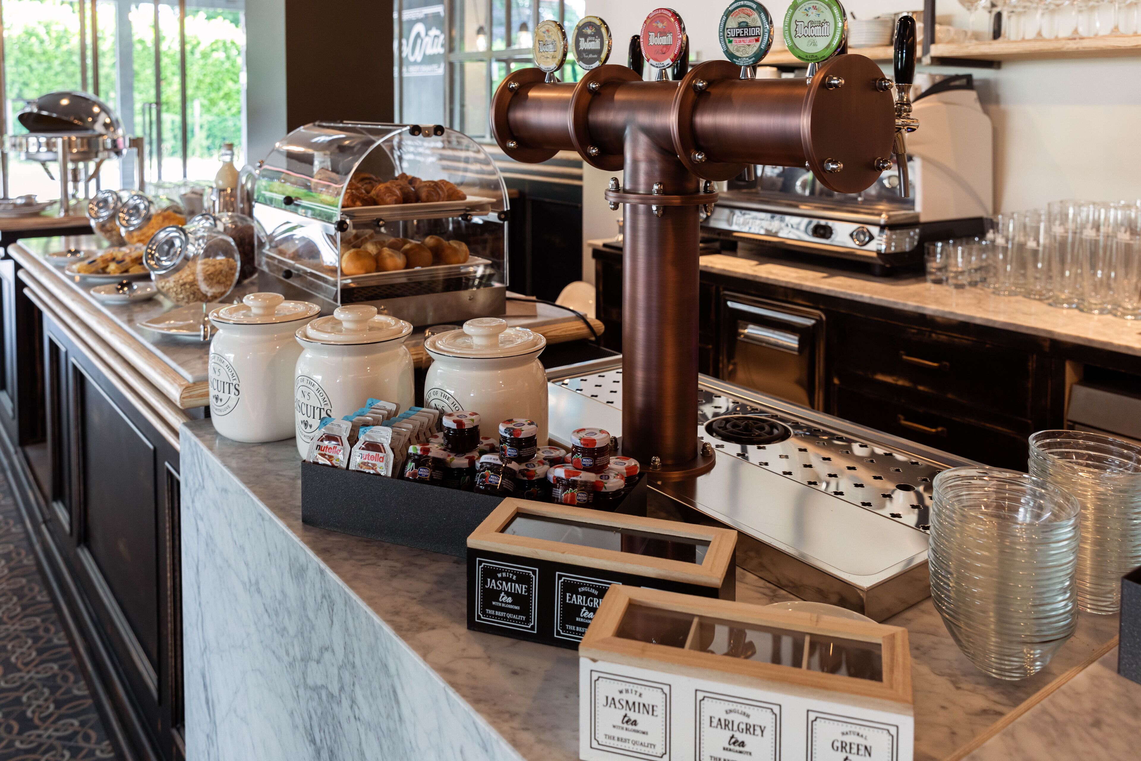 A breakfast bar with a coffee machine, tea dispensers, and a variety of food items.