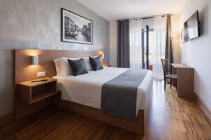 Una camera d'albergo moderna con un letto grande, comodini, una scrivania, una TV e una finestra con tende.