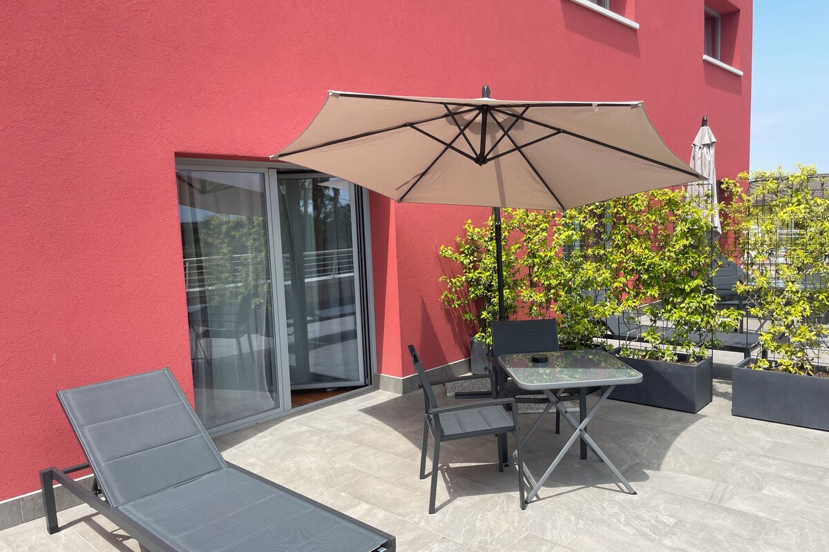 An outdoor patio with a table and chairs, a large umbrella, and a glass door leading to a balcony.