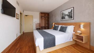 Una habitación de hotel moderna con una cama grande, suelo de madera, un armario, un televisor y un cuadro en la pared.